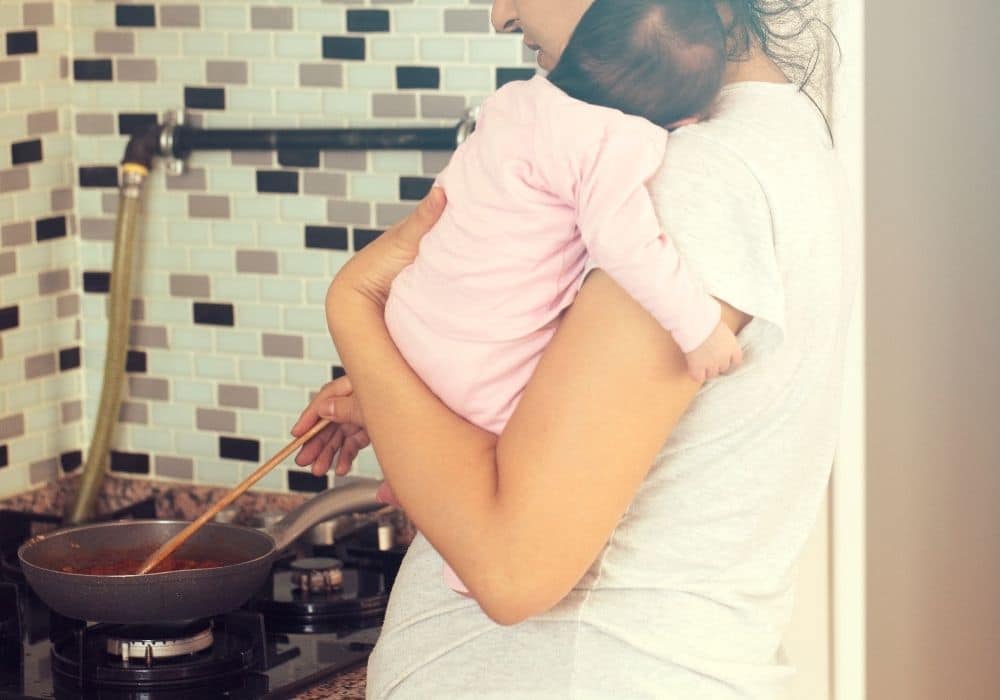 בדידות אחרי לידה אישה מבשלת אוכל עם תינוק